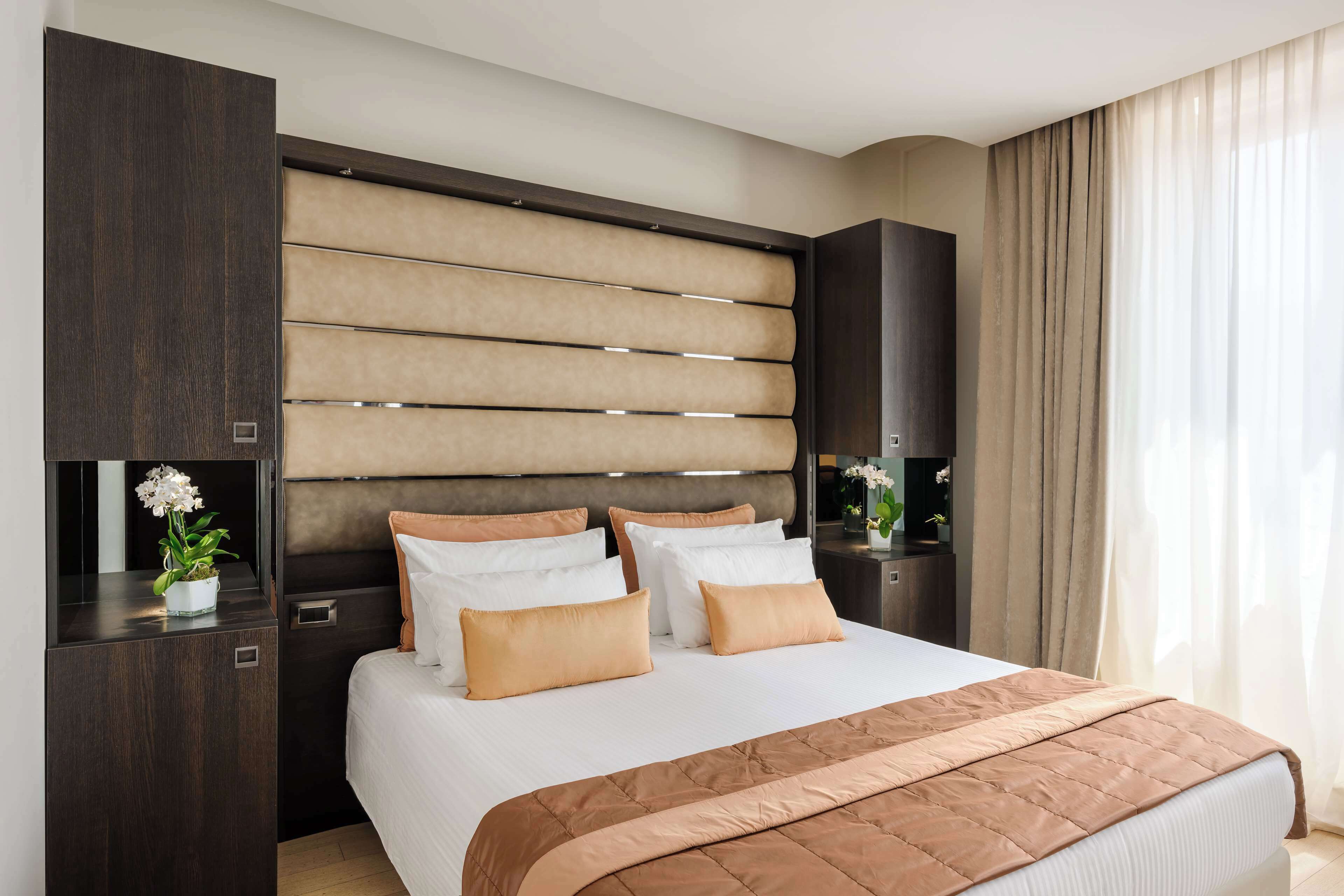 A modern bedroom with a large bed, dark wood headboard, and a beige accent wall.