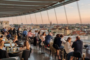 A rooftop restaurant with outdoor seating overlooking a cityscape.