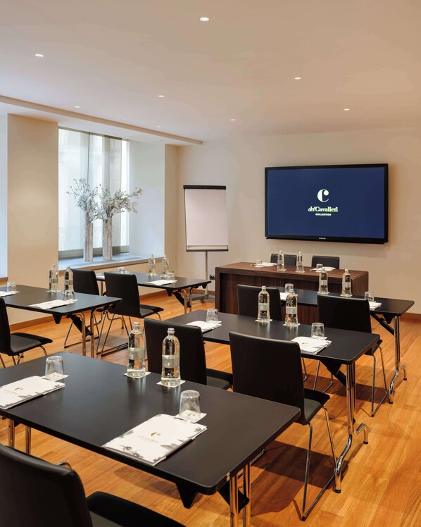 Un salón de conferencias con mesas, sillas, una pantalla de proyector y un ventanal con vistas.
