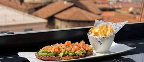 Un balcón con una mesa que sostiene un sándwich y papas fritas, con vista a un paisaje urbano que incluye un edificio con cúpula verde.