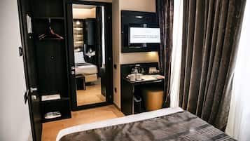 Una habitación de hotel con una cama, un escritorio con una silla, un televisor y un armario.