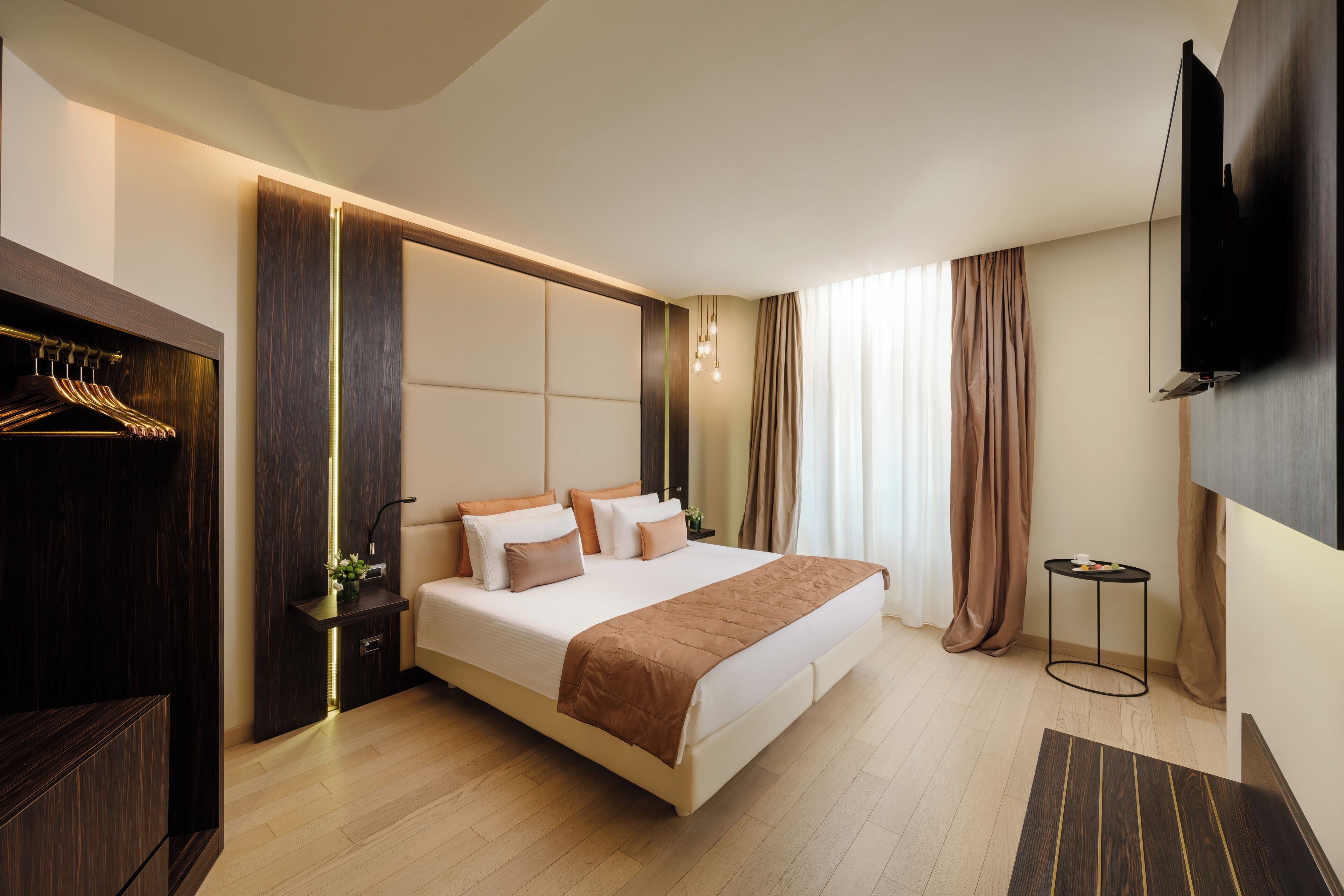 Une chambre d’hôtel moderne avec un grand lit, un téléviseur fixé au mur, une table de chevet et une armoire.