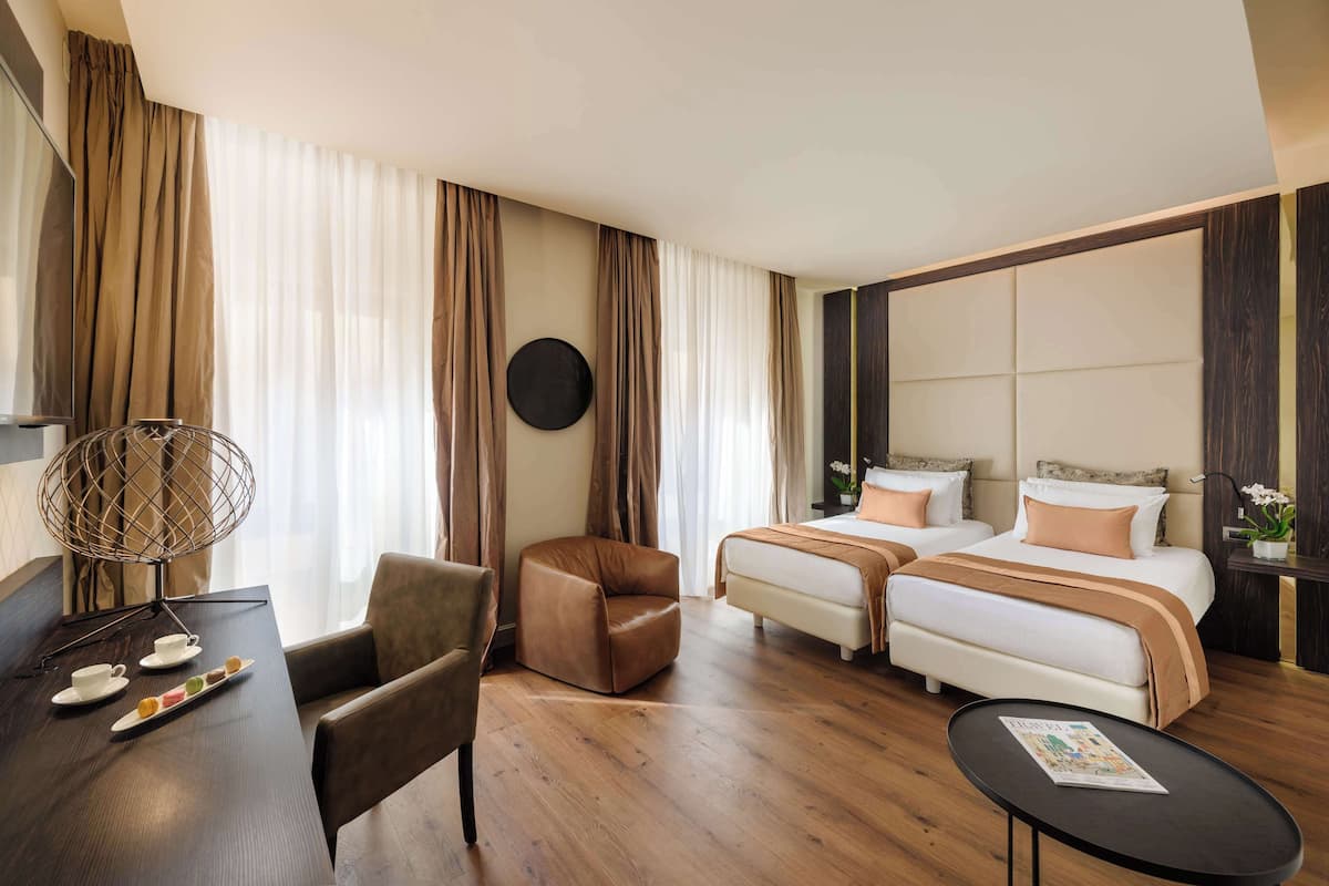 Ett hotellrum med en säng, två stolar, ett litet bord och ett runt bord med en tidning på.