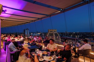 Zona pranzo all'aperto con tavoli e sedie, affacciata su una vista sulla città al crepuscolo.