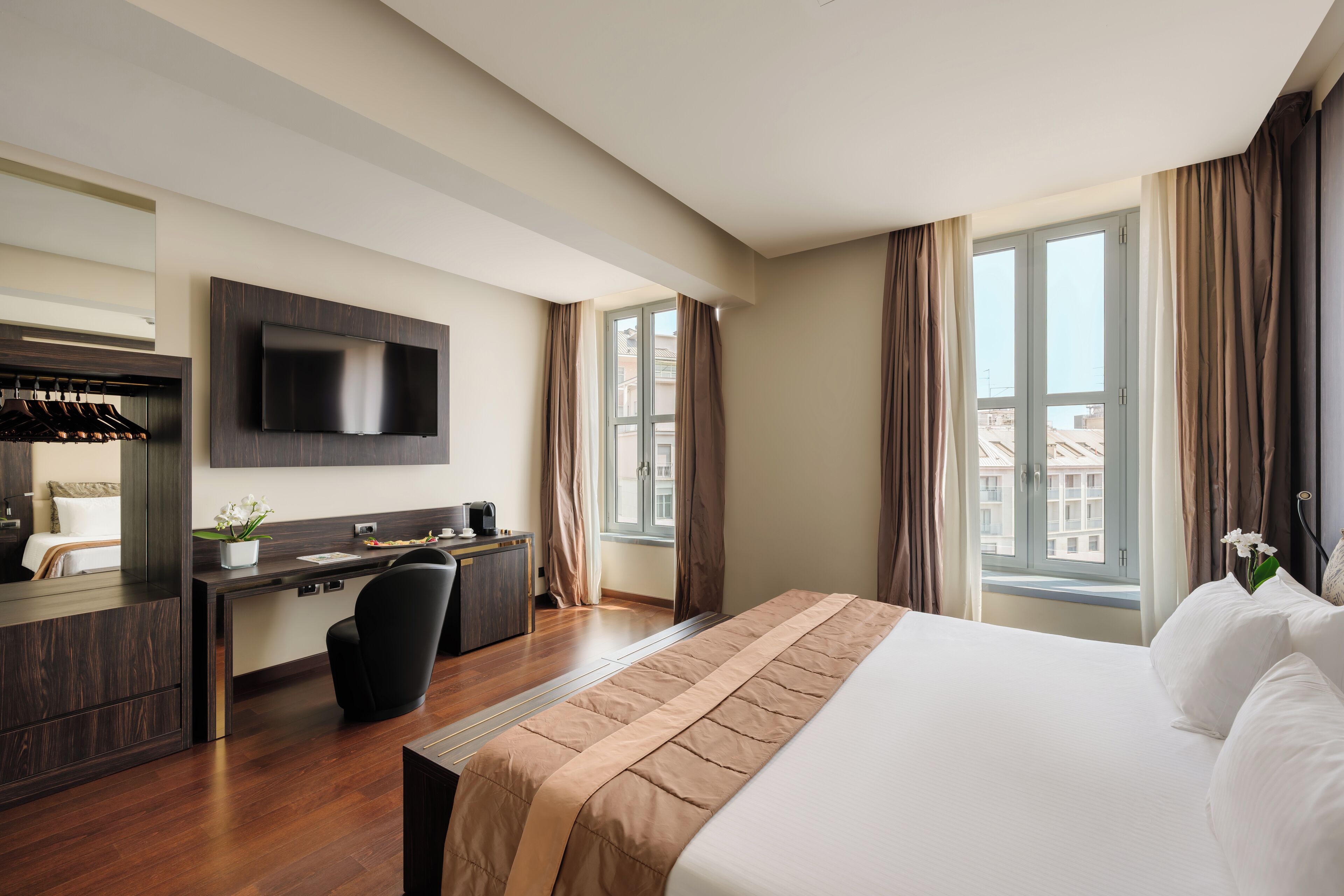 A modern hotel room with a large bed, a desk with a chair, a flat-screen TV, and a window with curtains.