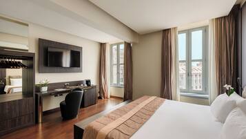 Una habitación de hotel moderna con una cama grande, un escritorio con silla, un televisor de pantalla plana y una ventana con cortinas.