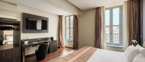 A modern hotel room with a large bed, a desk with a chair, a flat-screen TV, and a window with curtains.