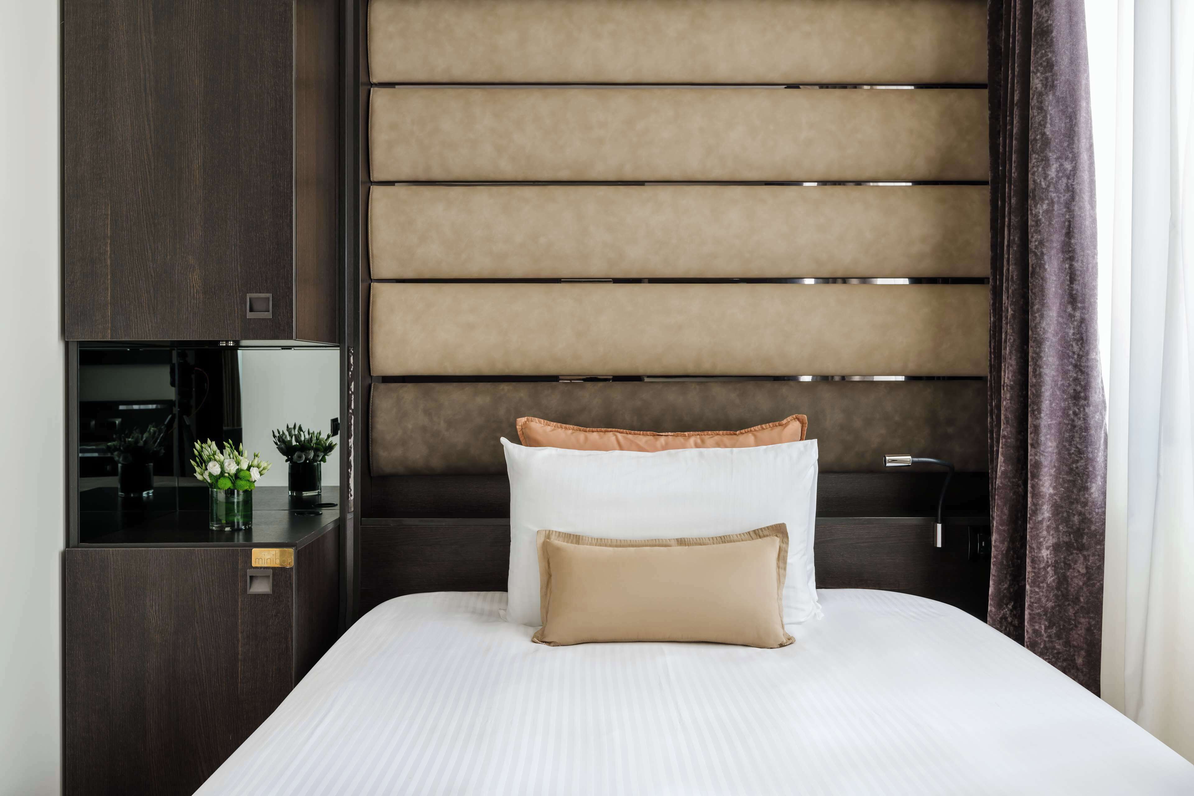 A neatly made bed with white and beige pillows, a dark wooden headboard, and a small bedside table with a lamp.