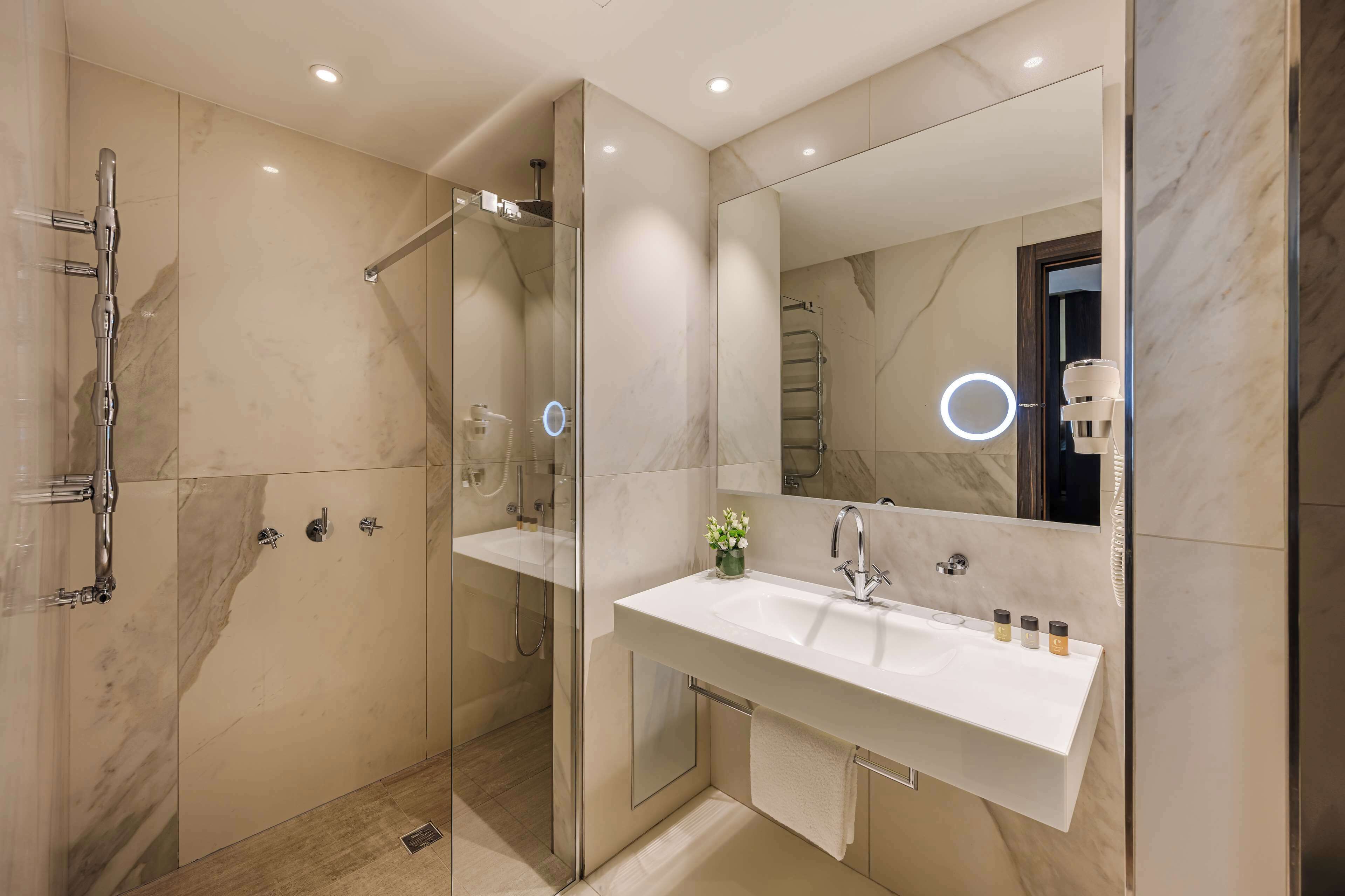 A modern bathroom with a glass-enclosed shower, a large mirror, and a white sink with toiletries.