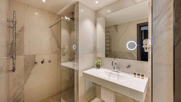 A modern bathroom with a glass-enclosed shower, a large mirror, and a white sink with toiletries.