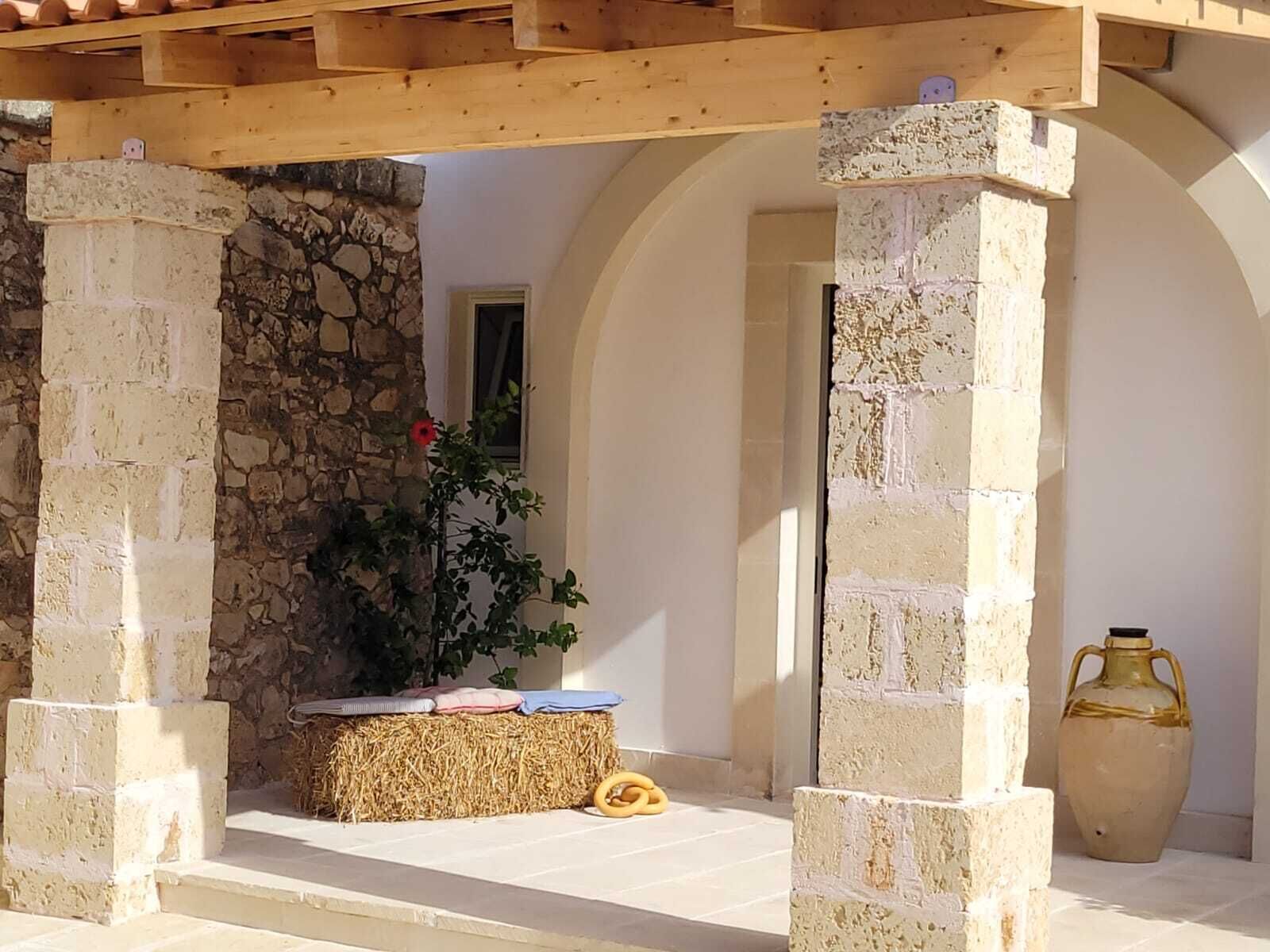 Un espace extérieur abrité, doté de murs en pierre, d’une pergola en bois et d’un banc en pierre agrémenté de coussins.