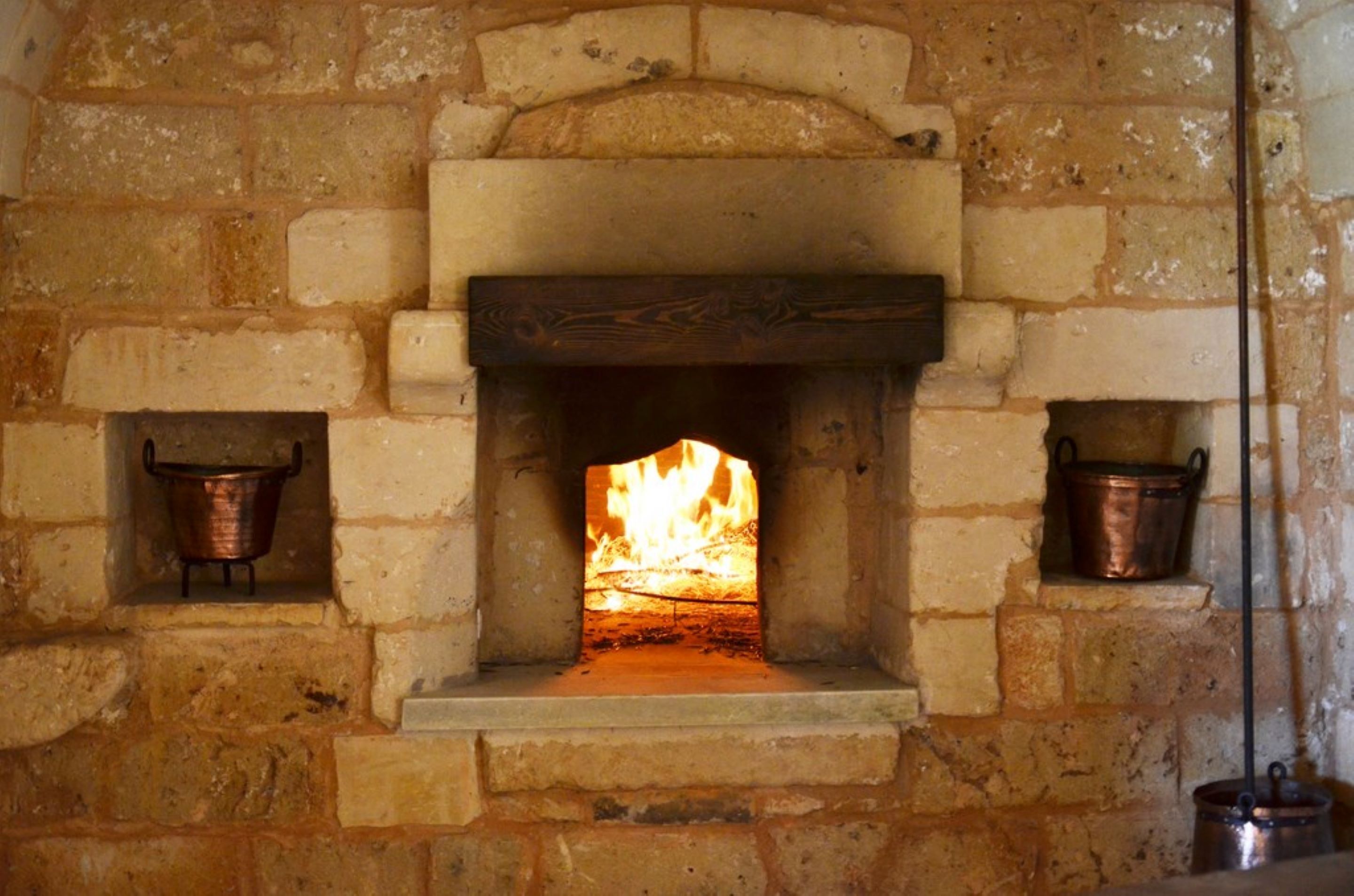 A stone fireplace with a fire burning inside, flanked by two copper pots on shelves.