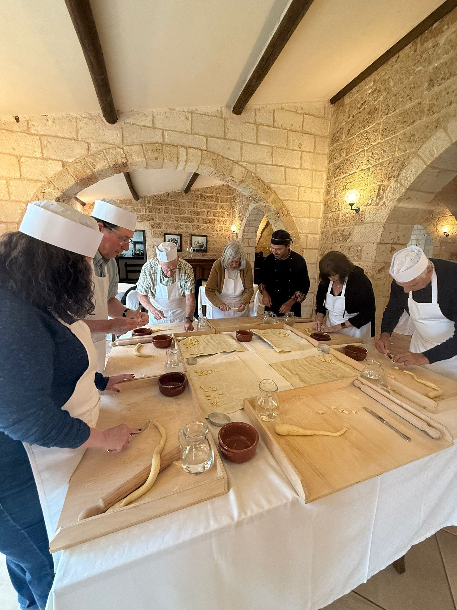 A group of people in aprons and chef hats working at a long table with baking tools and ingredients.