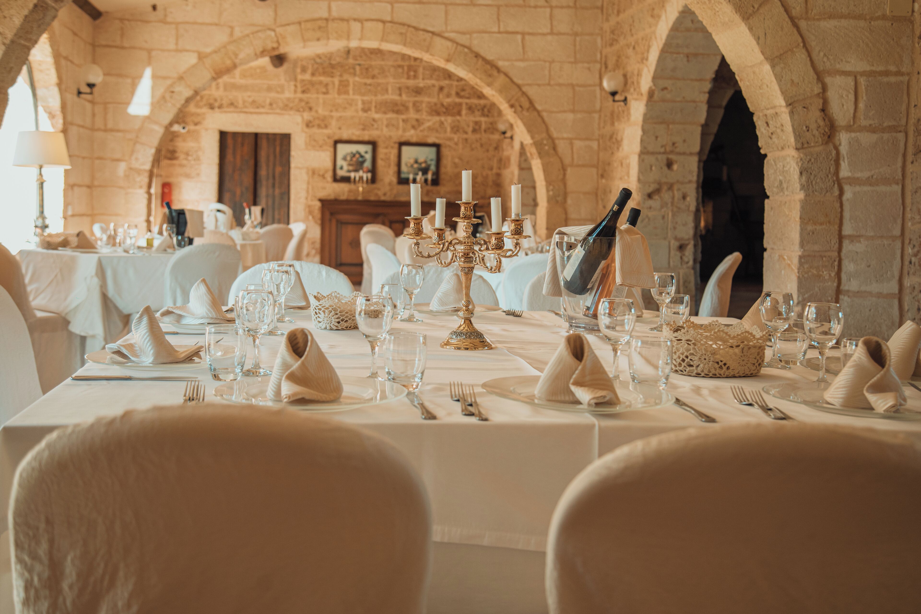 A dining area with tables set for a meal, featuring white tablecloths, glassware, and a candelabra centerpiece.