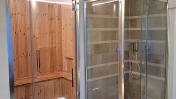A modern bathroom with a glass-enclosed shower, a wooden sauna, and a tiled floor.