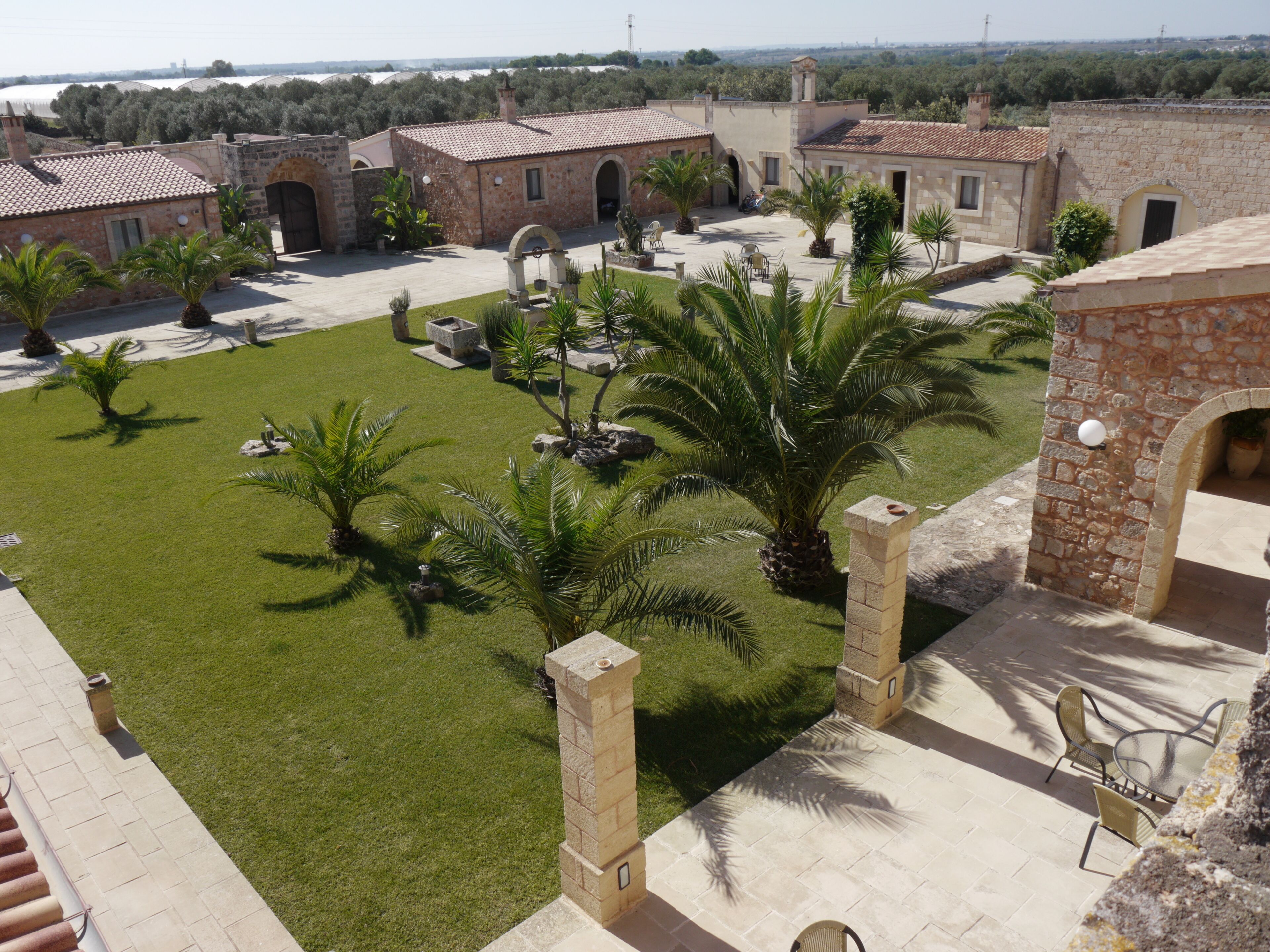 A courtyard with a well-maintained lawn, palm trees, and stone buildings with tiled roofs.