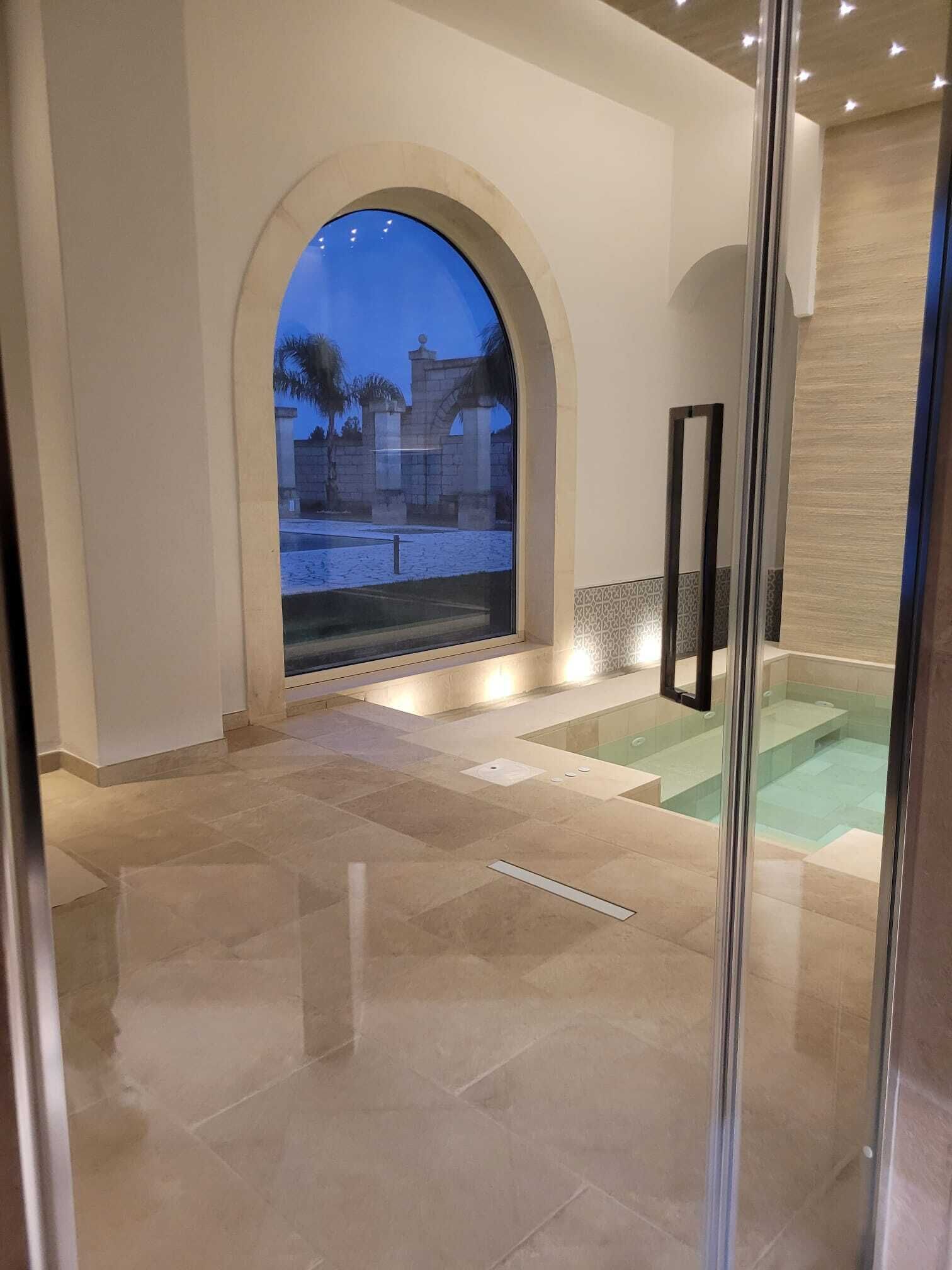 A modern interior with a glass door leading to a pool area, a stone archway, and a tiled floor.
