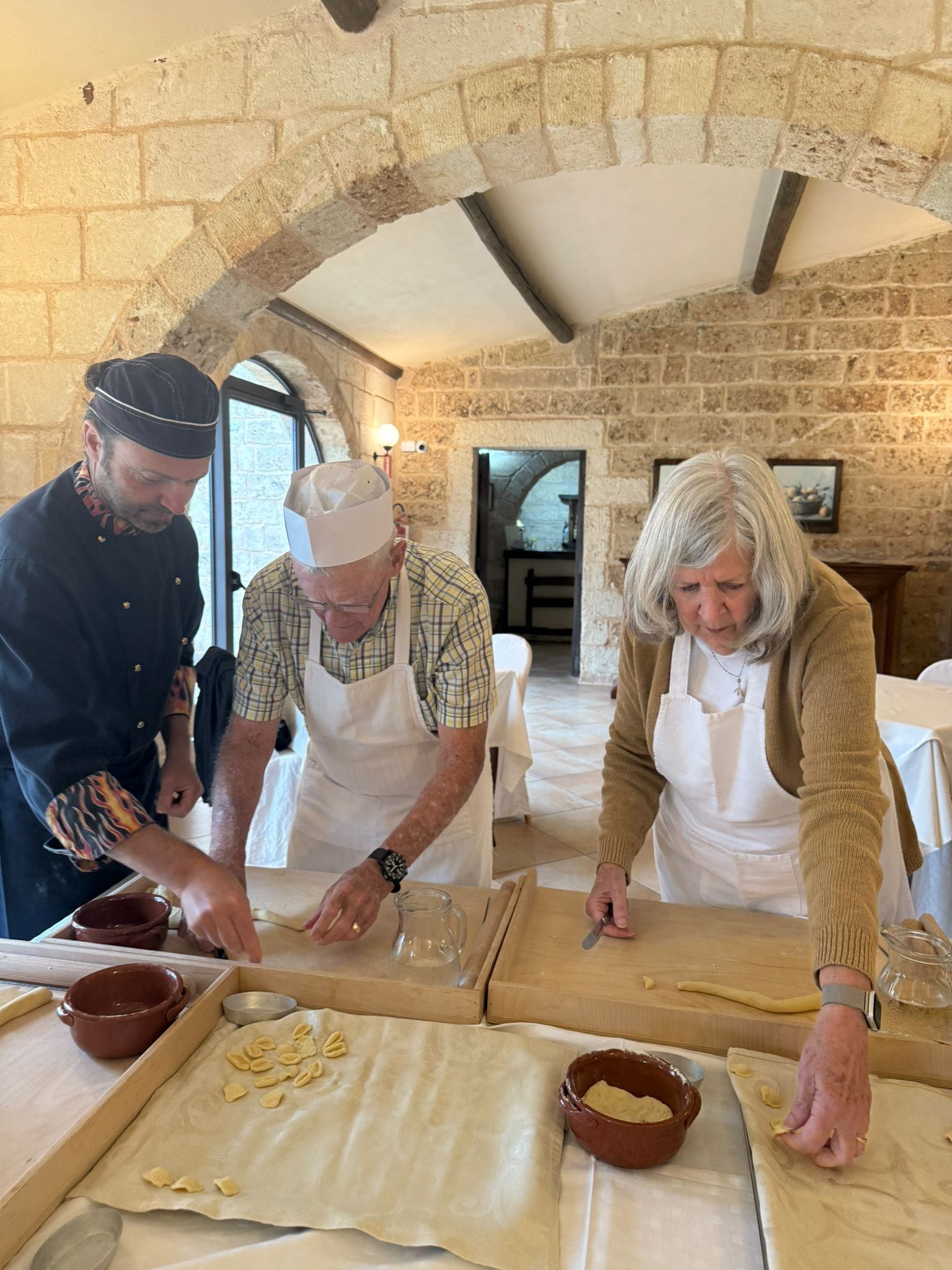 A group of people preparing food in a rustic kitchen with stone walls and a vaulted ceiling.