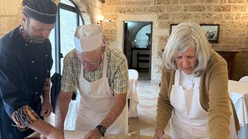 Un gruppo di persone prepara cibo in una cucina rustica con pareti in pietra e soffitto a volta.