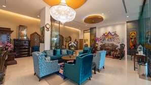 A spacious living room with a large chandelier, blue patterned sofas, and a traditional wooden cabinet. - Rimkhobfa Urban Resort (Samut Prakan)