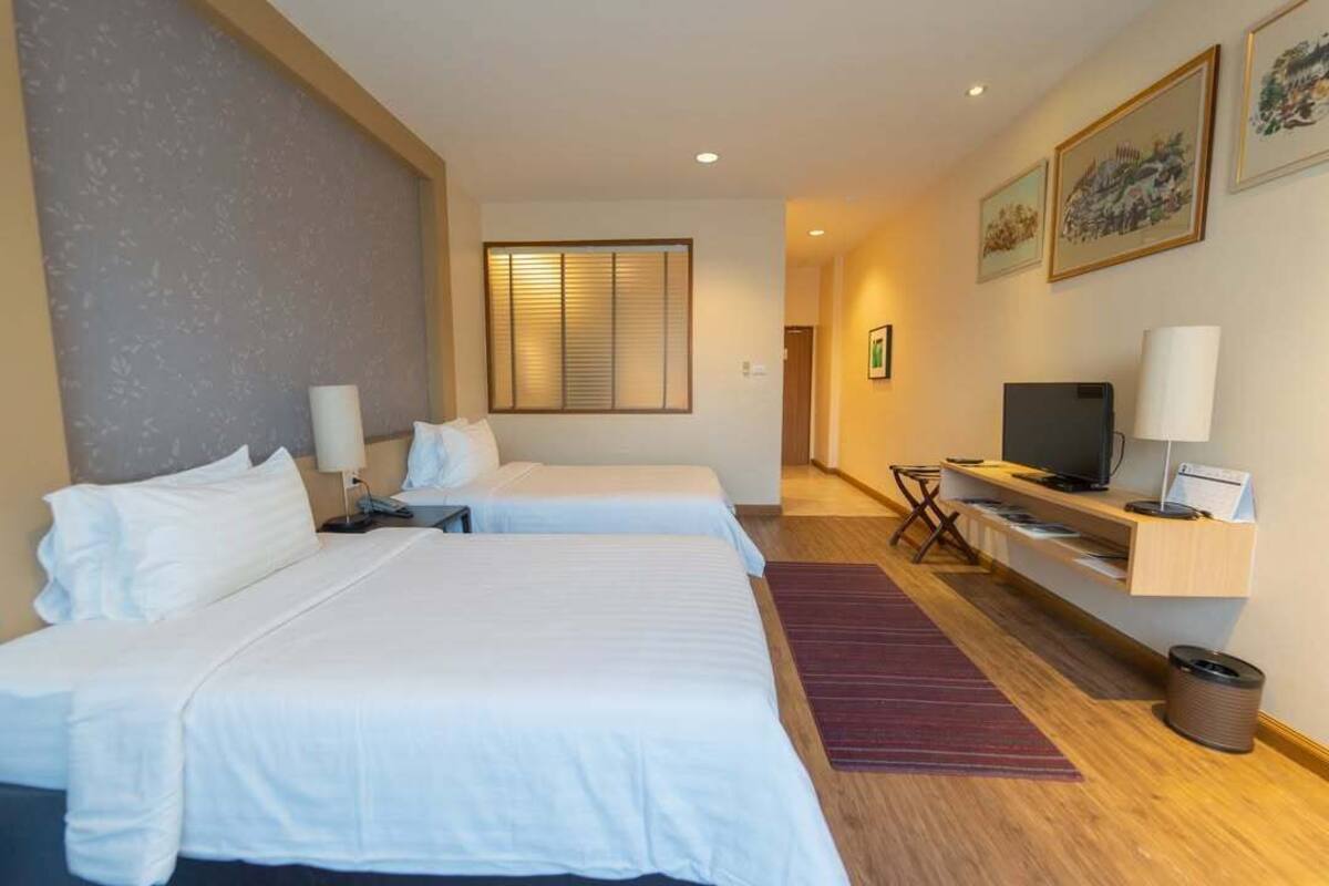 Een hotelkamer met twee bedden, een televisie, een bureau en een raam met zonwering.