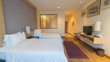 Una habitación de hotel con dos camas, televisión, escritorio y ventana con persianas.