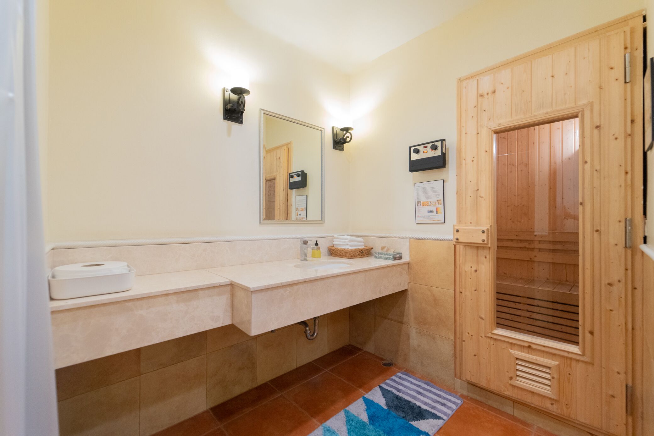 A bathroom with a wooden sauna door, a sink with a towel dispenser, and a mirror.