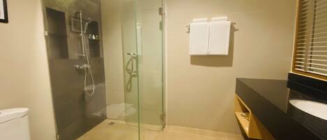 Un baño moderno con ducha de vidrio, inodoro blanco y lavamanos negro sobre encimera oscura.
