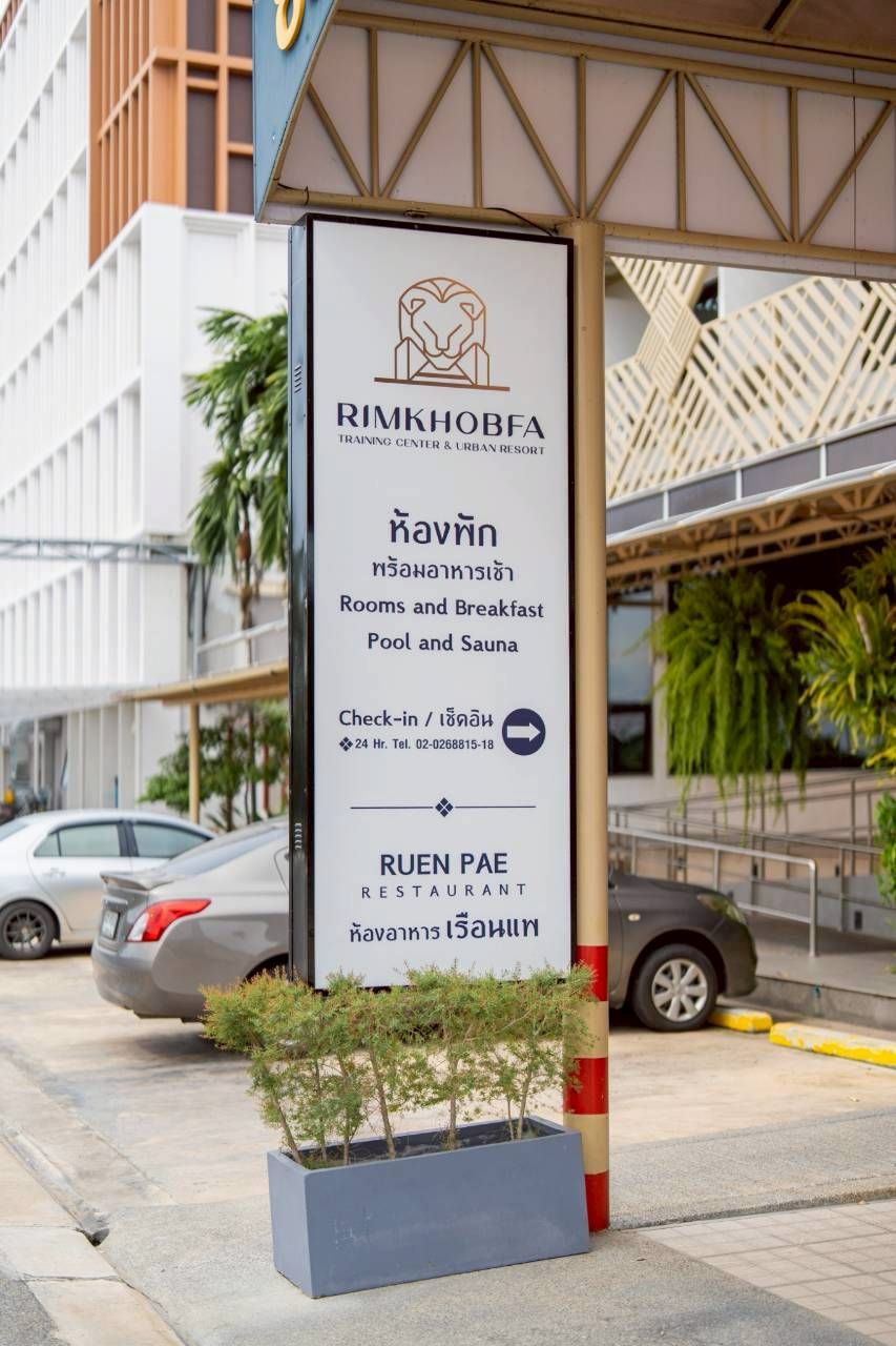 A signboard for RIMKHOBFA TRAINING CENTER & URBAN RESORT with amenities like rooms, breakfast, pool, and sauna.