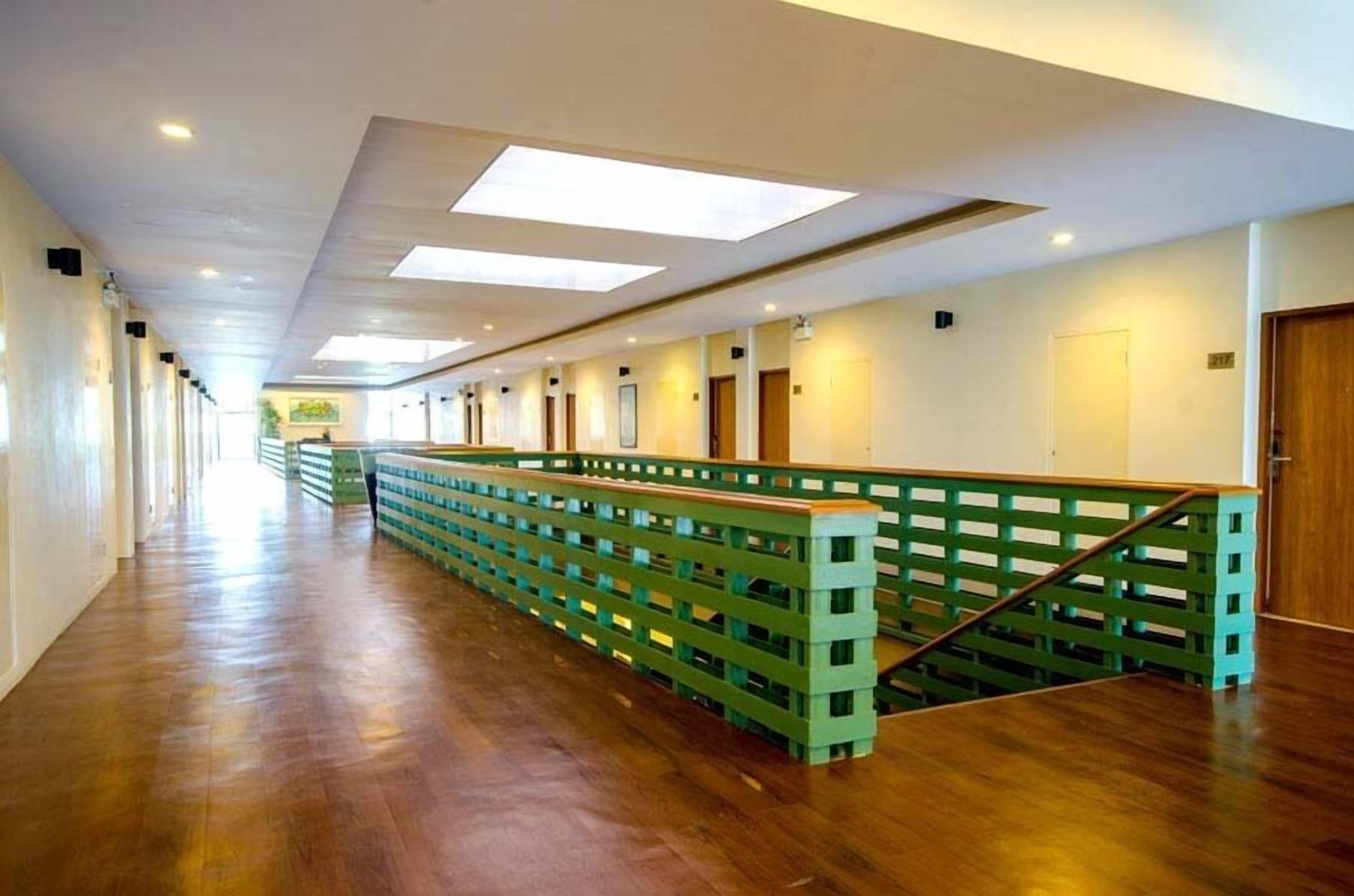 Un pasillo largo y estrecho con pisos de madera y barandillas verdes, que conduce a varias puertas.
