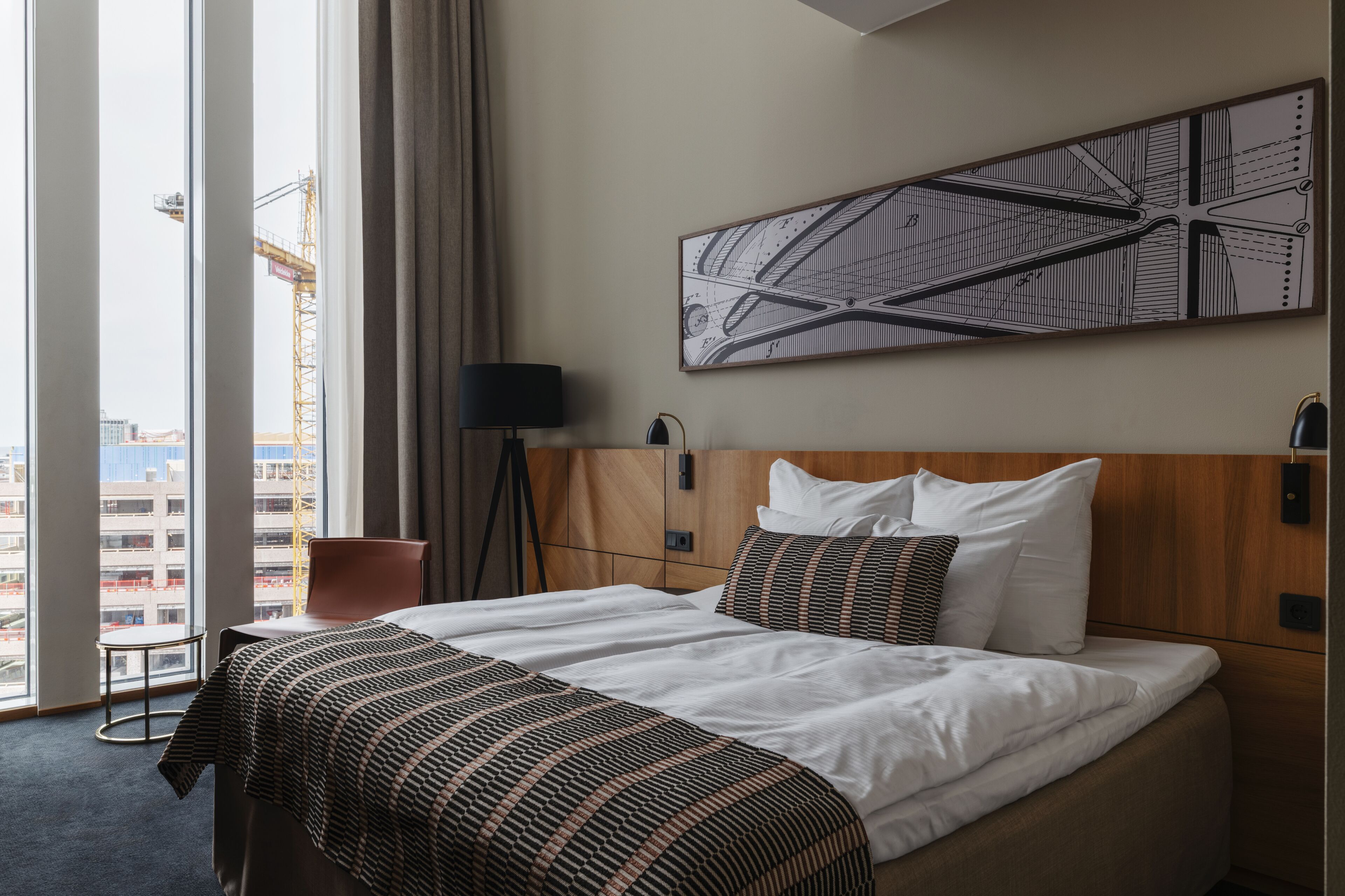 A hotel room with a large bed, a view of the cityscape, a modern abstract painting, and a lamp.
