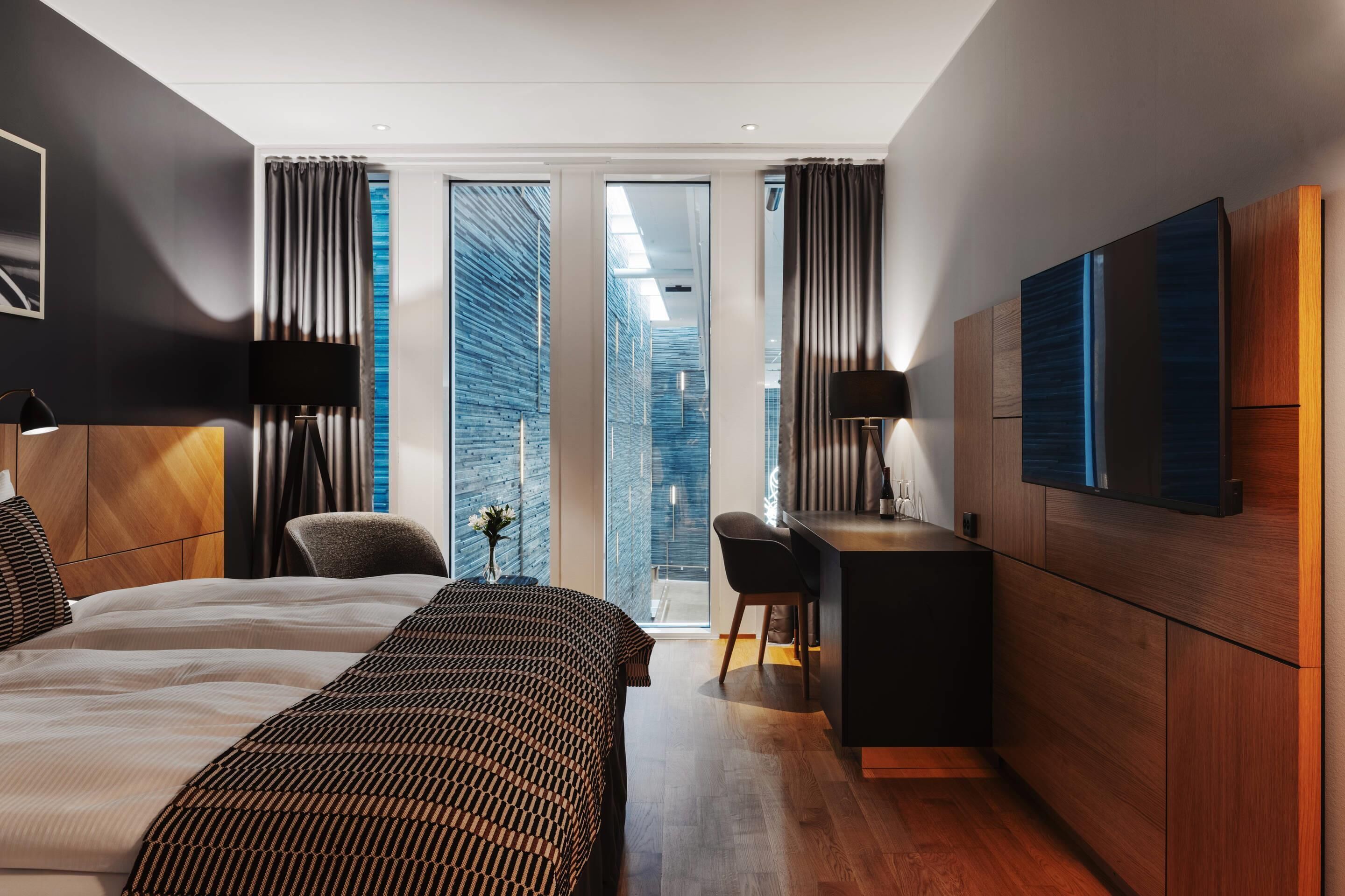 A modern hotel room with a large bed, a desk, and a TV.