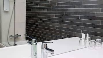 Un baño moderno con un lavabo blanco, dos grifos cromados, un cabezal de ducha de mano y una pared revestida de baldosas oscuras.