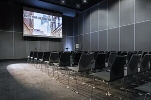 A conference room with rows of chairs, a large screen displaying a presentation, and a framed picture on the wall.