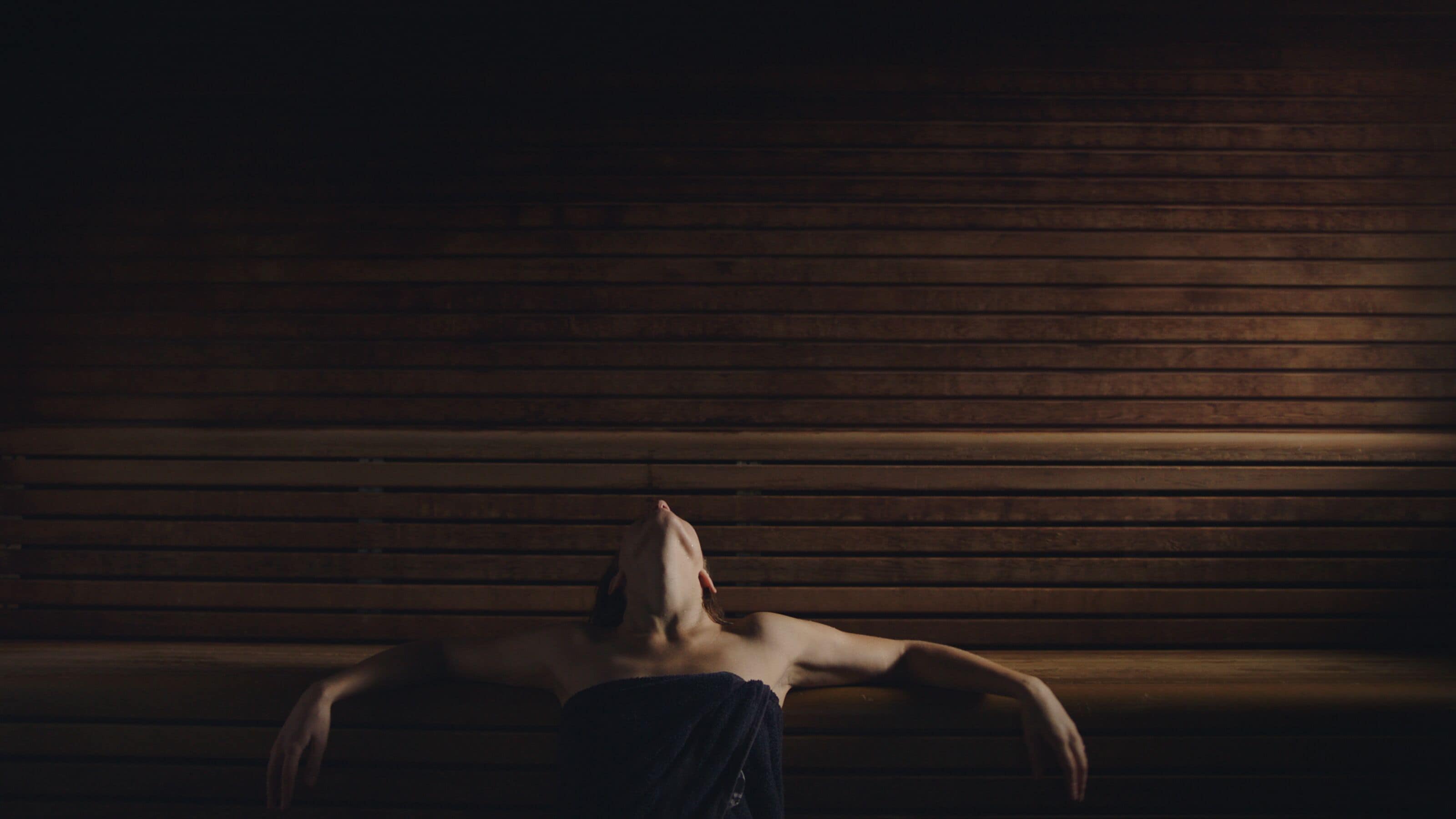 A person lying on a bench in a dimly lit room with wooden paneling.