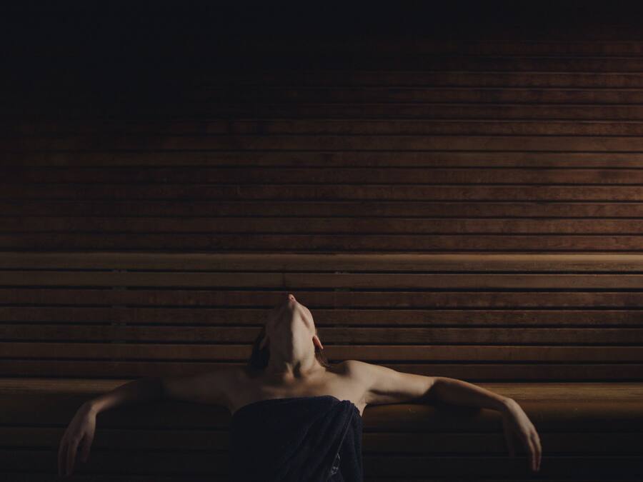 A person lying on a bench in a dimly lit room with wooden paneling.