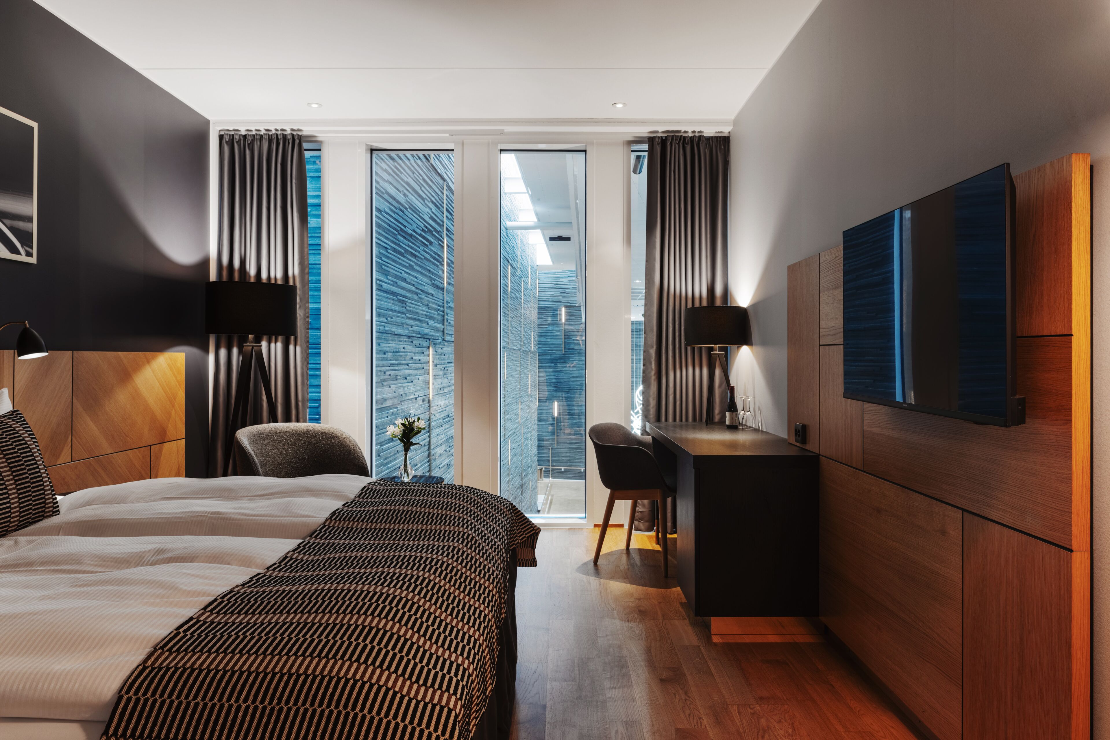 A modern hotel room with a large bed, a desk, and a TV.