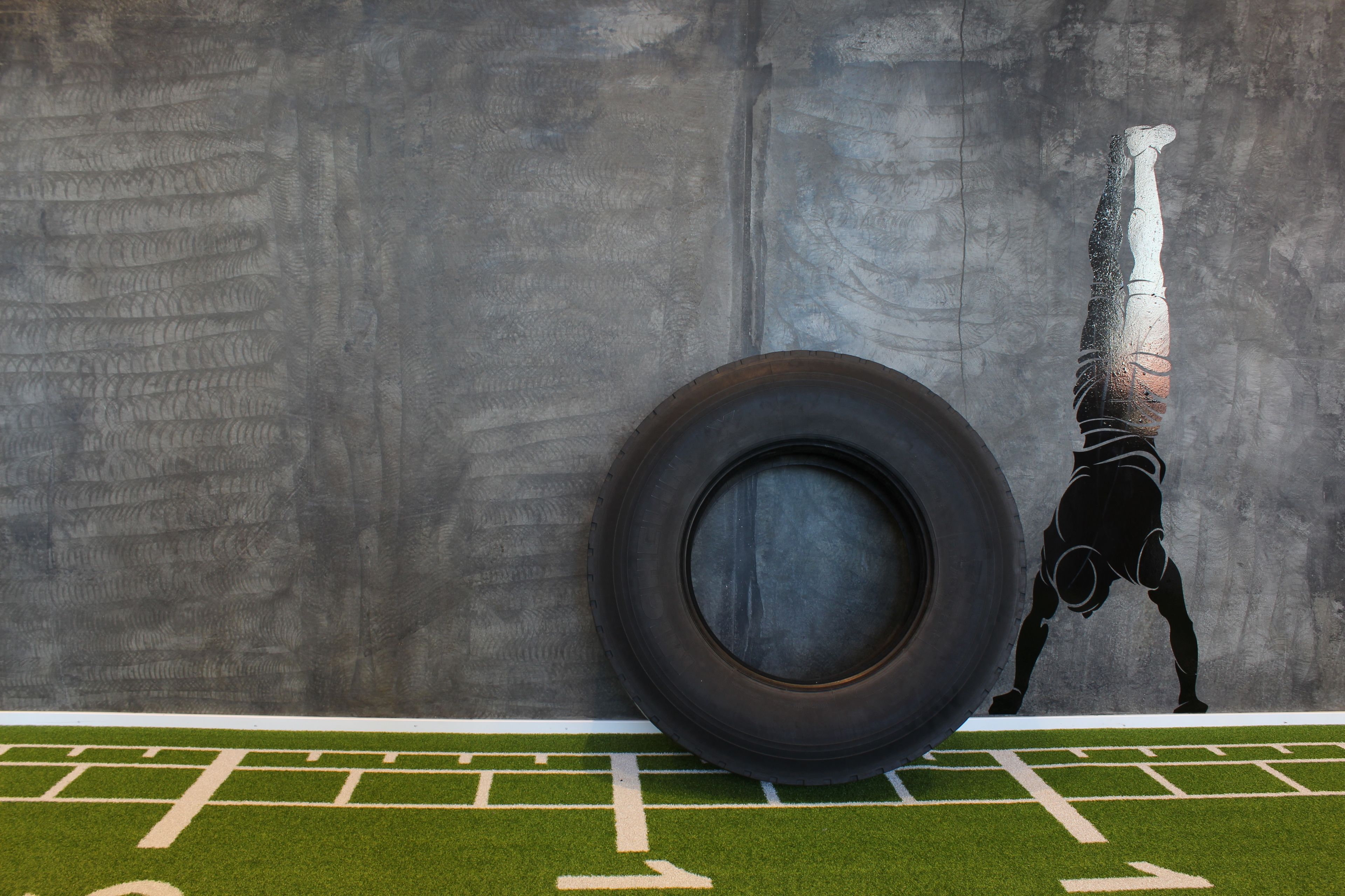 A person performing a handstand against a wall with a tire and a football field layout.