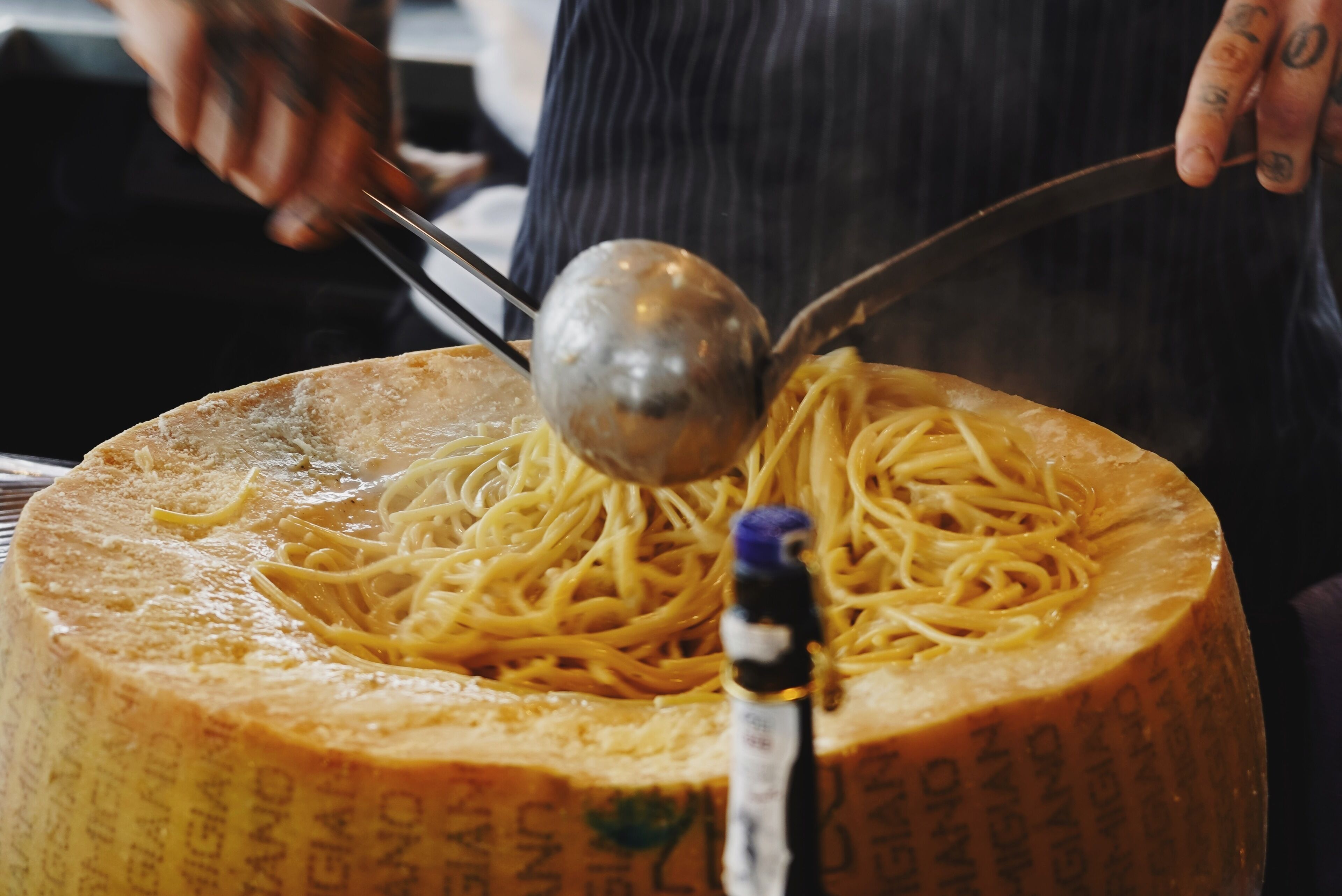 A large wheel of cheese with a ladle of spaghetti on top.