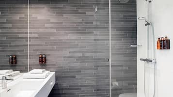 A modern bathroom with a grey brick wall, a glass shower enclosure, a white sink, and toiletries on the wall.