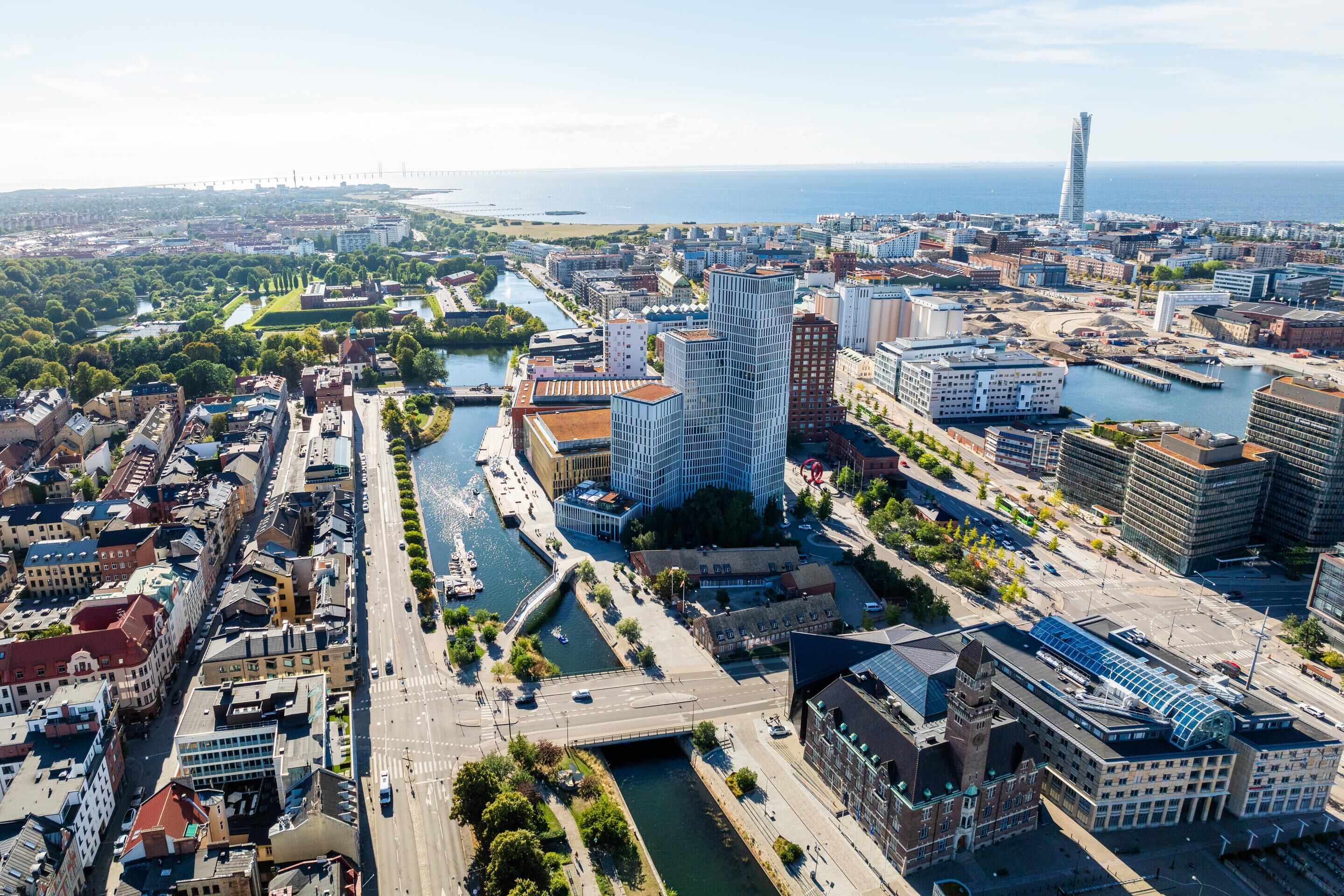 Vista aérea de un paisaje urbano con un río, edificios modernos y una torre distintiva.