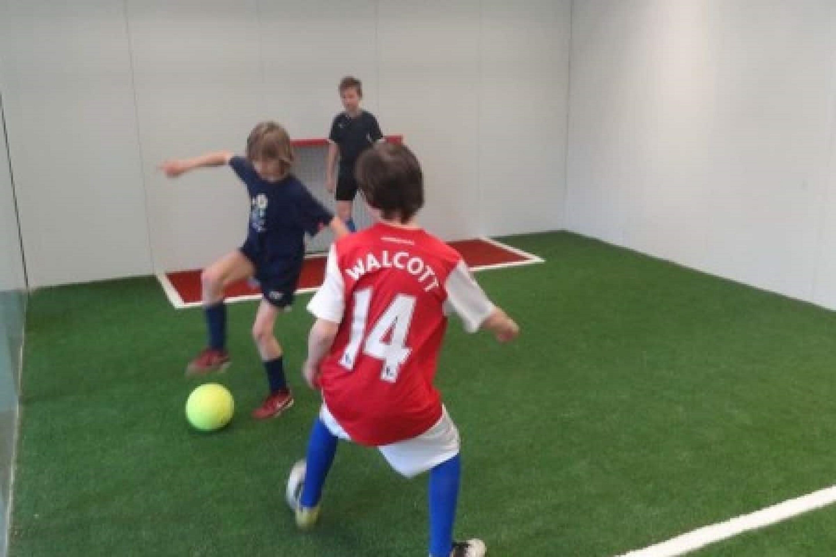 Un match de football qui se déroule sur un terrain intérieur recouvert de gazon synthétique, avec des poteaux de but.