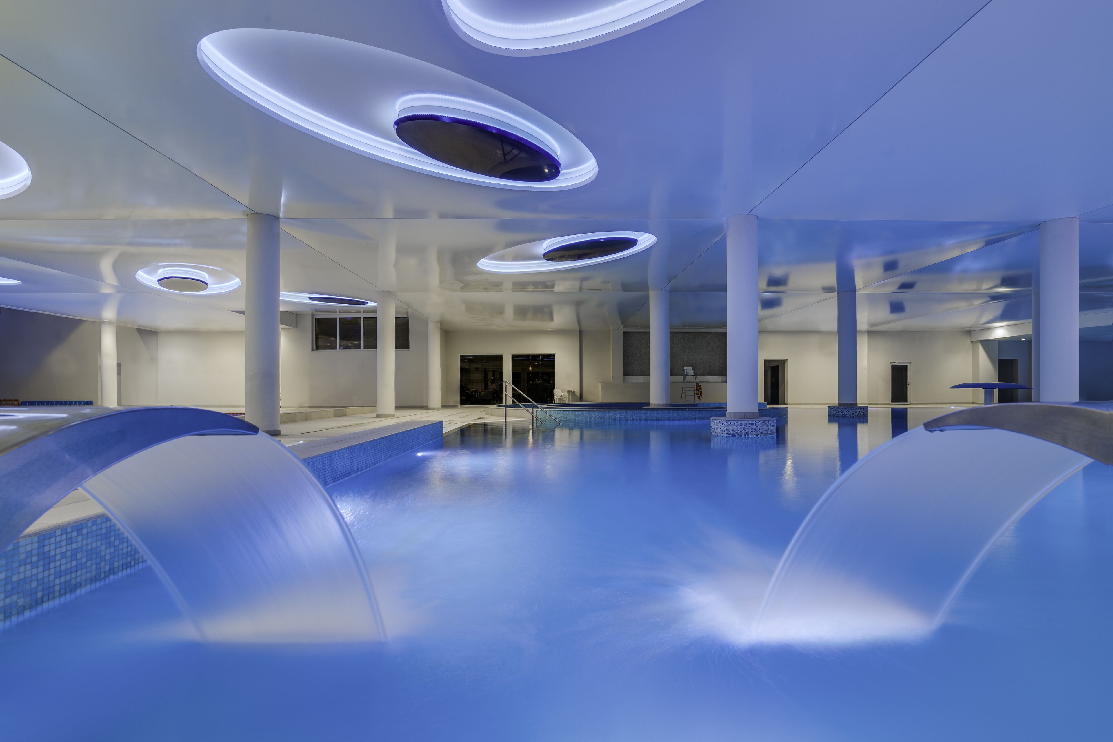 Una piscina interior moderna con luces circulares en el techo y una vista despejada del área de la piscina.