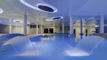 Une piscine intérieure moderne, dotée de luminaires circulaires au plafond et offrant une vue dégagée sur l’ensemble de l’espace piscine.