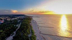An aerial view of a coastal city at sunset with a beach, a road, and buildings. - Grand Lubicz - Uzdrowisko Ustka (Ustka)