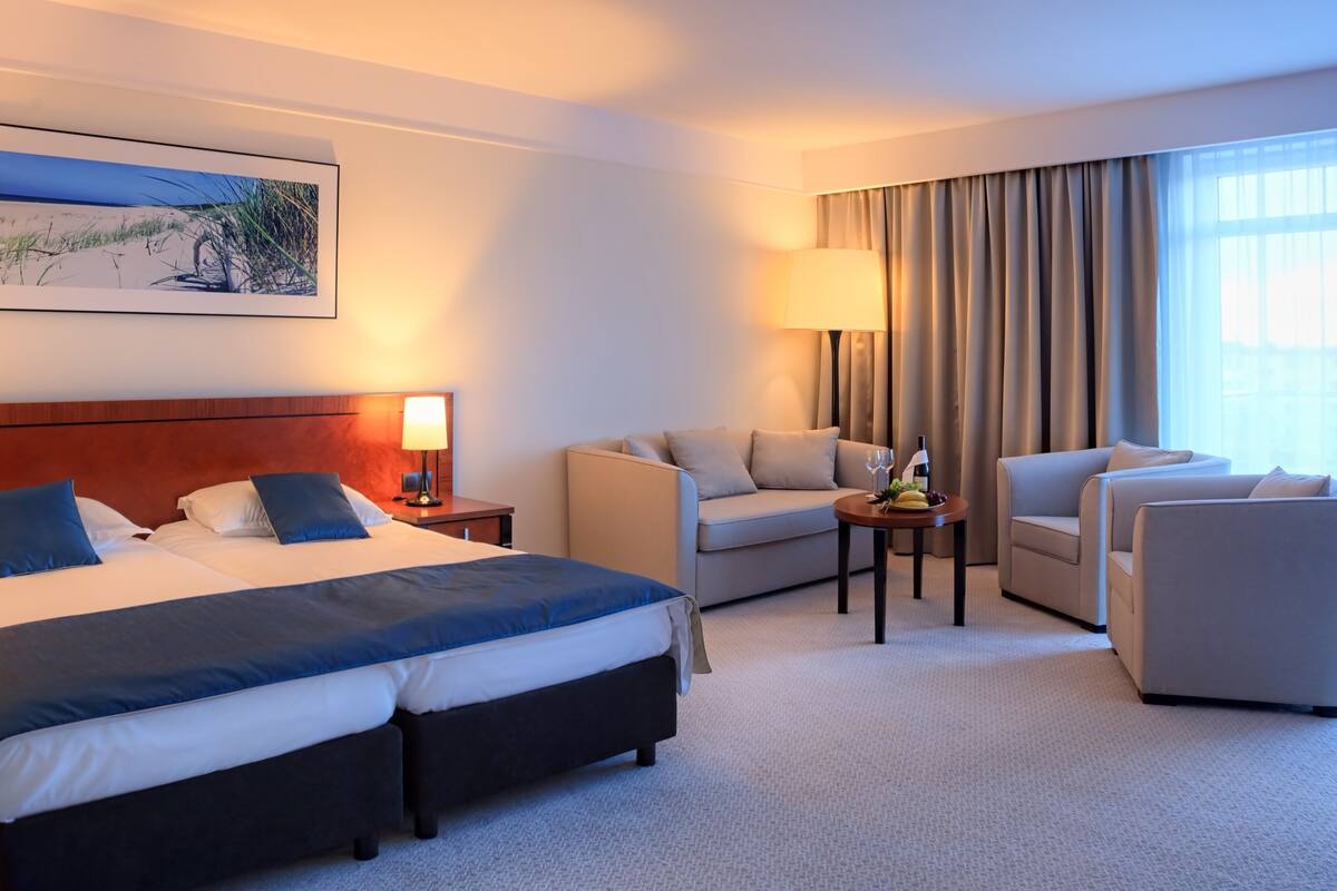 A hotel room with a large bed, two sofas, a small table with a lamp, and a painting on the wall.