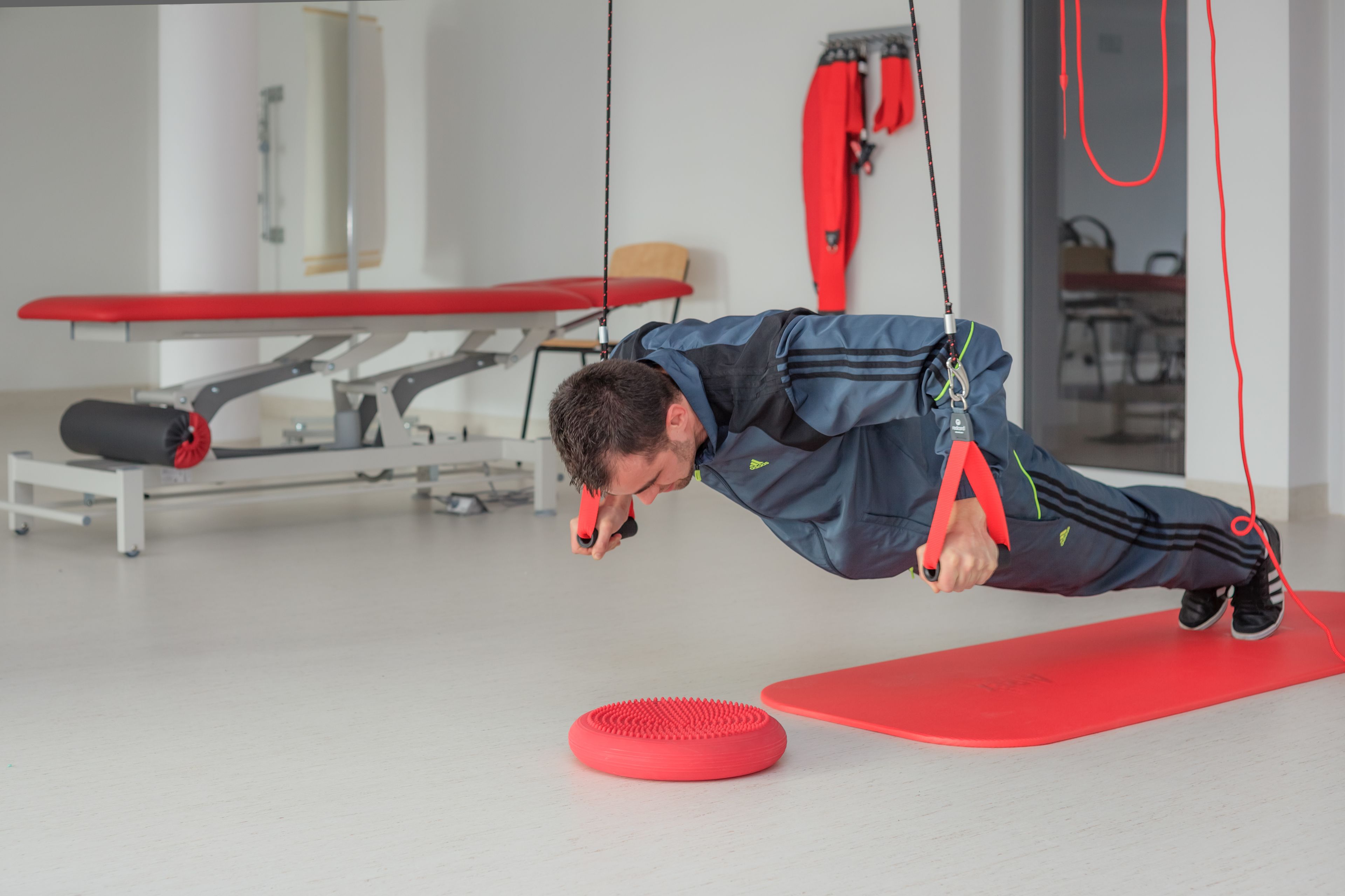 A person performing a stretching exercise on a red mat in a room with a red bench and a white wall.