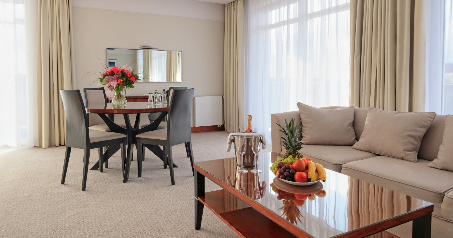 A hotel room with a dining area, a sofa, and a coffee table with fruit.