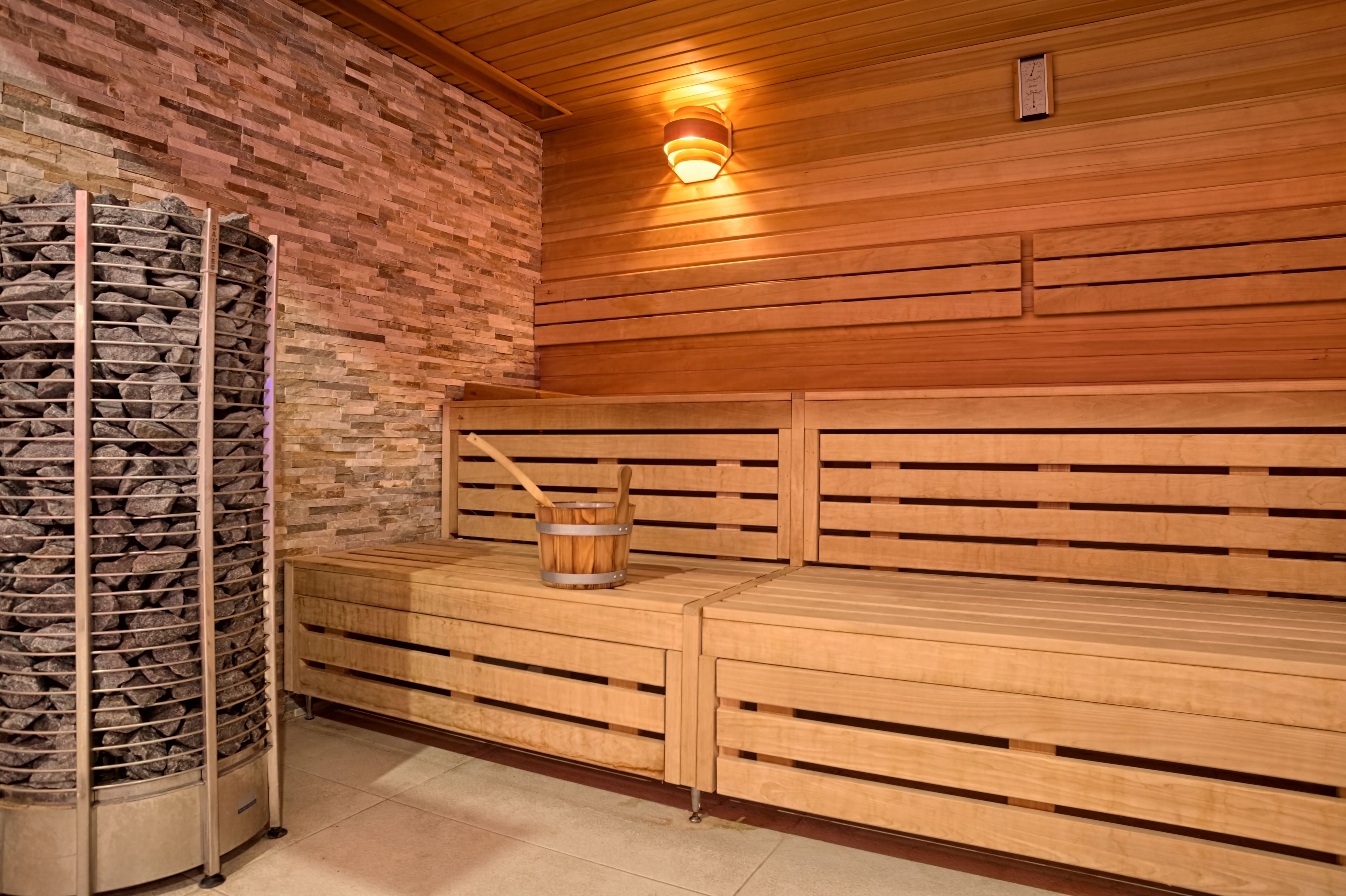 A sauna with wooden benches, a stone wall, and a wooden ceiling.