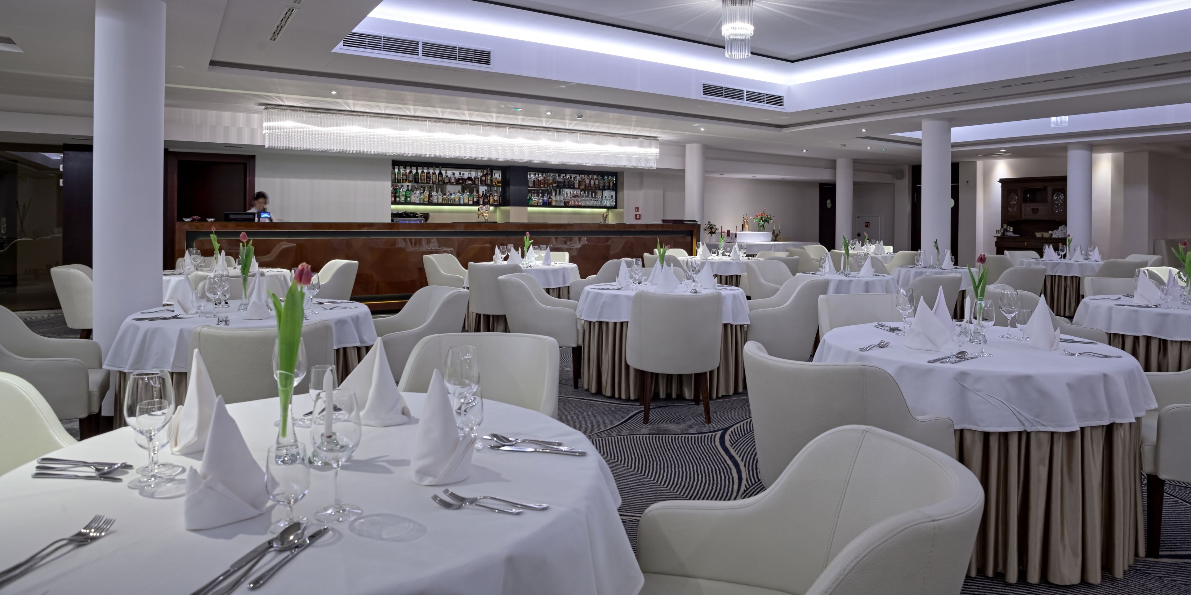 A restaurant with round tables set for dining, a bar area, and a reception desk.